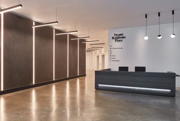 Minimalist office lobby with a reception desk and a wall behind it displaying 'Twenty Rathbone Place' along with a list of floors and occupants, including 'Flashtalking', 'Hive', and 'Pixelogic'. The design is clean and modern.