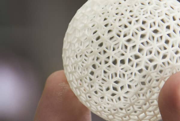 A close-up of a person holding a lightweight, 3D-printed sphere with a hexagonal lattice design. The intricate pattern showcases the details of the structure, emphasizing its geometric elegance.