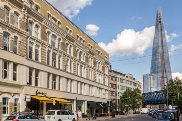 untitled-81 Street view featuring a multi-story refurbished building with ornate architecture and large windows, a ground-floor storefront named 'Lantana' with a yellow awning, and The Shard skyscraper visible in the background under a partly cloudy sky.