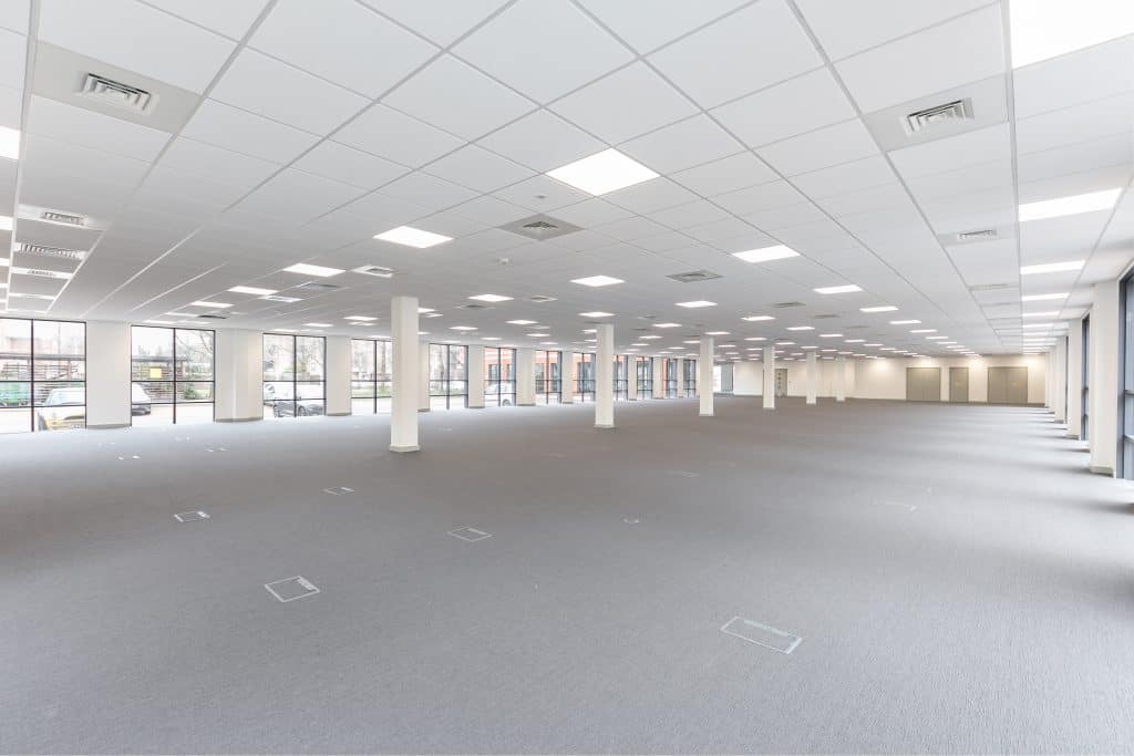 commercial fitout - Virtus Modern open-plan office interior showcasing professional fit out and refurbishment work, featuring natural light from large windows, grid ceiling with recessed lighting, white walls, and grey carpet—ideal for commercial workspace transformation.
