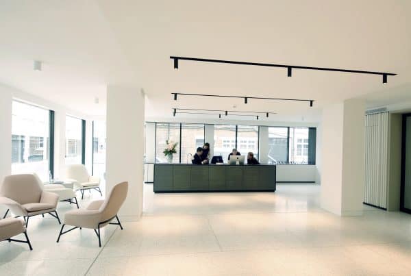 Spacious office reception area with minimalist seating, natural light from large windows, and sleek black ceiling lighting—demonstrating premium commercial fit out and modern workplace refurbishment.