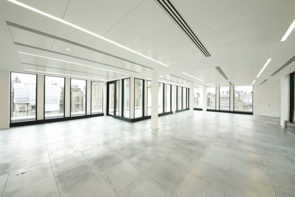 Cat A Fitout A spacious and bright interior of a CAT A office space featuring large floor-to-ceiling windows that provide ample natural light. The minimalist design includes a smooth, polished concrete floor and a clean white ceiling with integrated lighting. The open layout enhances the feeling of airiness, making it an ideal environment for various uses, from creative workspaces to modern offices. The view outside showcases an urban landscape, adding to the ambiance of the space.