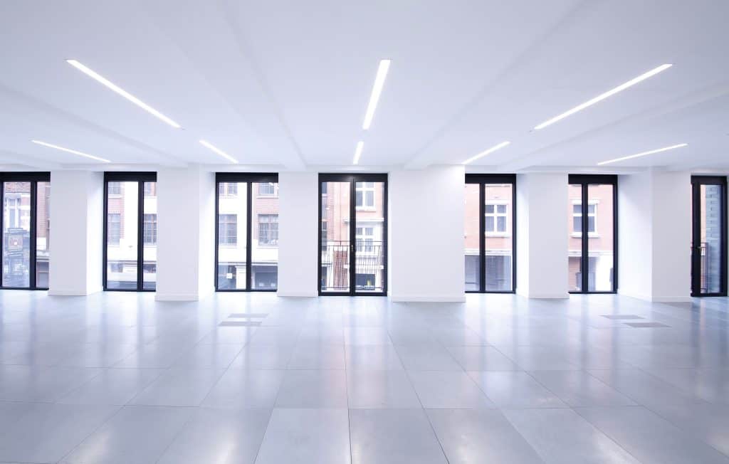 Design Trends and Innovations in Commercial Fitouts Spacious, modern empty room with white recessed ceiling lights, large light gray tiled floor, and floor-to-ceiling black-framed windows offering a view of exterior buildings