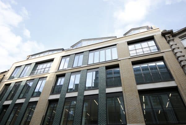 Exterior of a modern multi-story building, with a recently added upward extension with a brick facade, large tall windows on each floor, and slanted windows on the top floor.