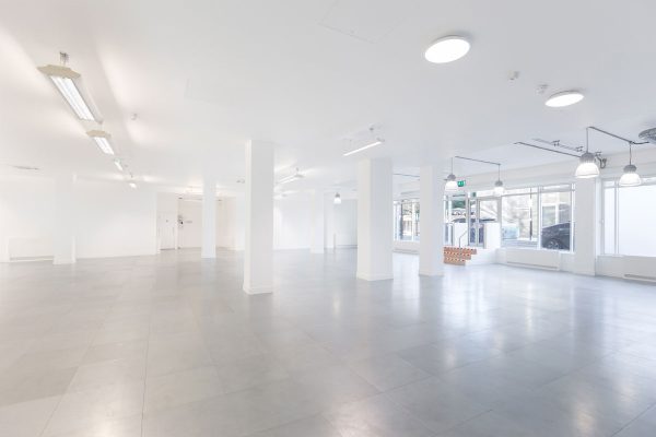 1-4 A spacious, open-plan interior featuring a bright, minimalist design with white walls and polished gray flooring. Tall columns provide structural support while maintaining an airy feel, enhanced by ample natural light streaming through large windows. The layout is versatile, allowing for various uses, from commercial to creative spaces, showcasing a clean and modern aesthetic ideal for customization and collaboration.