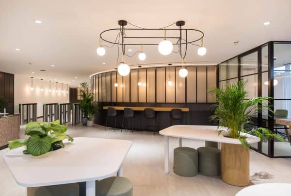 Bright, modern office lounge area transformed through a recent fit-out, featuring suspended circular light fixtures, a sleek counter with bar seating, and integrated planting—part of a refurbishment focused on creating inviting, multifunctional breakout zones.