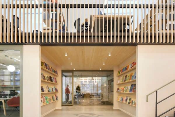 Modern publishers office with meeting room in the background, meeting room to the left of the image and stairs to the right leading to a mezzanine workspace.