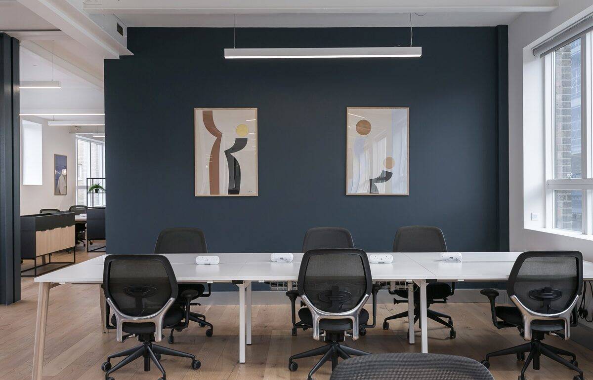 Office space featuring a sleek white desk setup, modern black chairs, and a bold blue accent wall with abstract artwork.