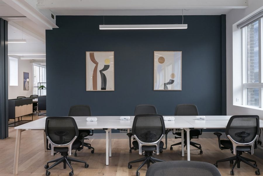 Office space featuring a sleek white desk setup, modern black chairs, and a bold blue accent wall with abstract artwork.