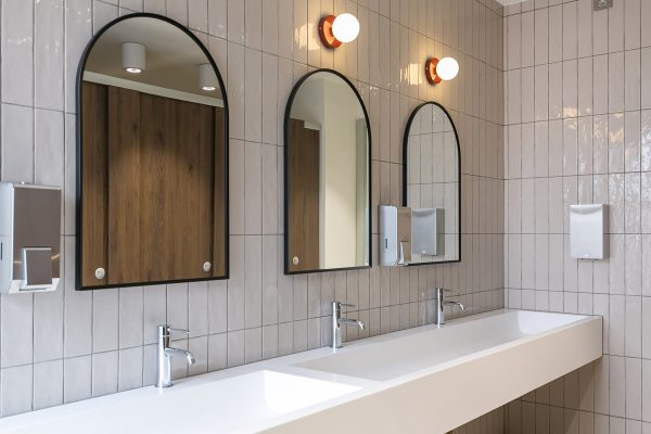 Bright restroom with a long white trough sink, multiple chrome faucets