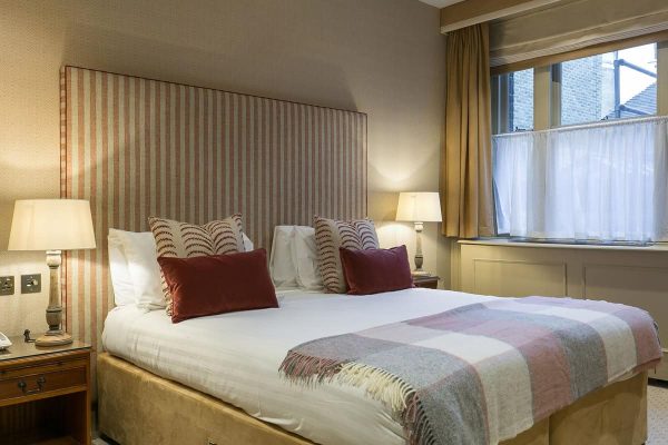 Bedroom with king-size bed, striped headboard, and red accent cushions. Warm beige walls and traditional bedside tables. Refurbishment could introduce contemporary color schemes and smart bedside lighting.