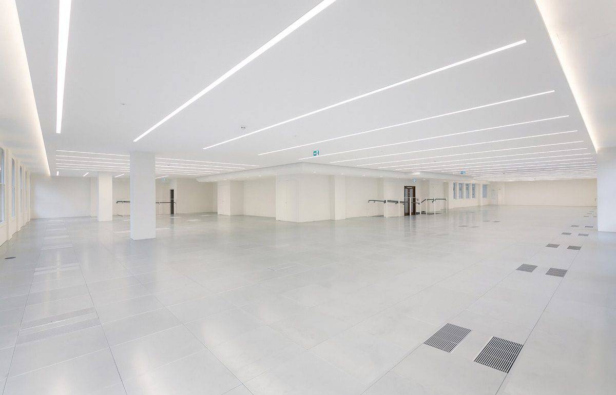 Spacious CAT A office interior showcasing advanced underfloor air distribution, intelligent lighting strips, and a neutral color palette for a contemporary workspace.