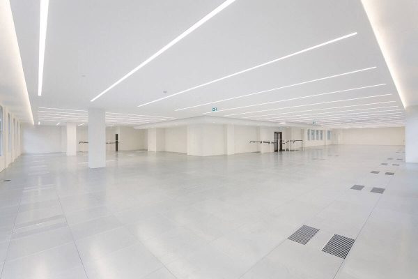 1-5 Spacious CAT A office interior showcasing advanced underfloor air distribution, intelligent lighting strips, and a neutral color palette for a contemporary workspace.