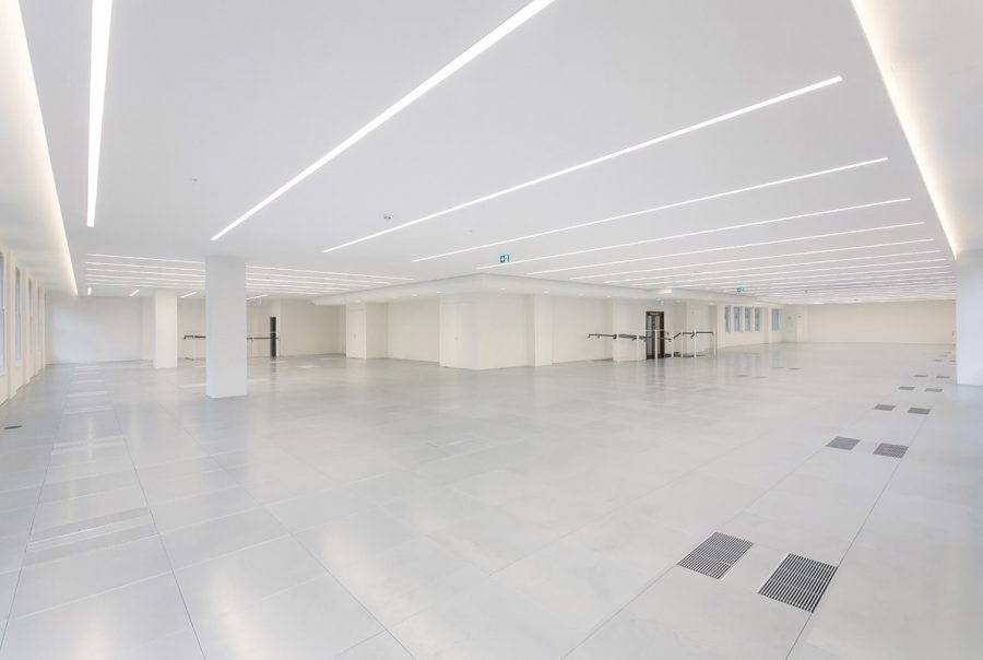 Spacious CAT A office interior showcasing advanced underfloor air distribution, intelligent lighting strips, and a neutral color palette for a contemporary workspace.