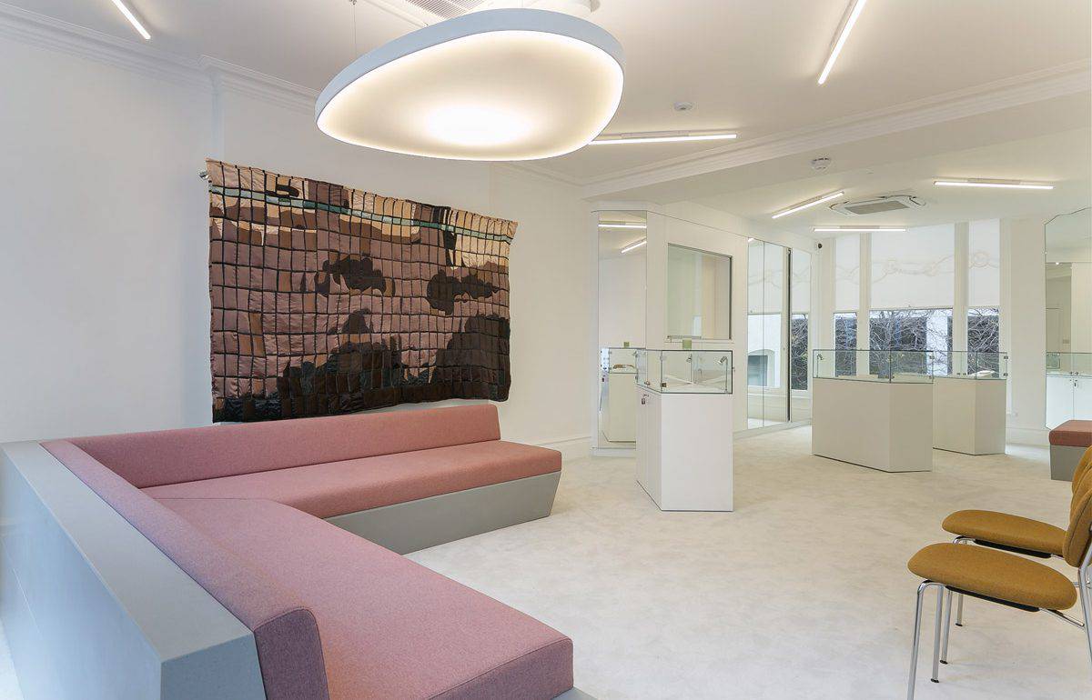 Wide-angle view of the refurbished showroom featuring bespoke seating, glass display units, and integrated lighting solutions. The design combines soft furnishings with hard finishes for a balanced, modern aesthetic. Pendant lighting and mirrors enhance brightness and spatial perception.