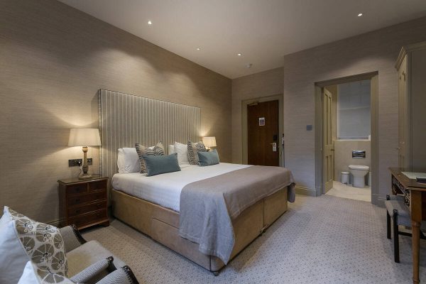 Bedroom with king-size bed, neutral décor, and view into en-suite bathroom. Classic furniture and soft lighting create a traditional feel. Refurbishment could focus on open-plan design and modern finishes.