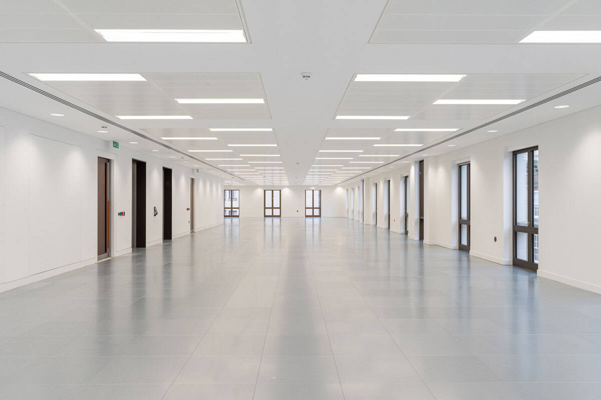Modern refurbished office level showcasing new lighting, smooth grey flooring, crisp white finishes, and updated window frames throughout