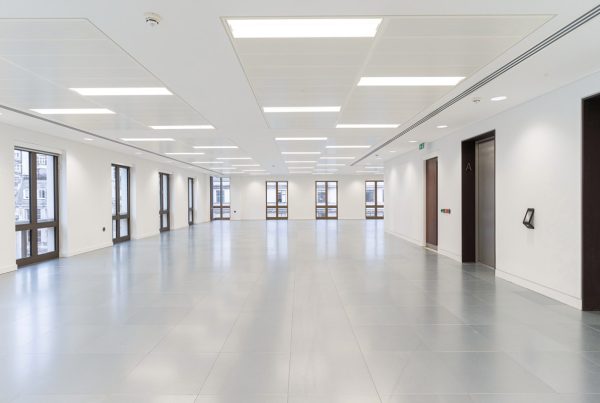 Open refurbished office space with sleek grey flooring, new lighting, crisp white walls, and updated lift entrances along the side.