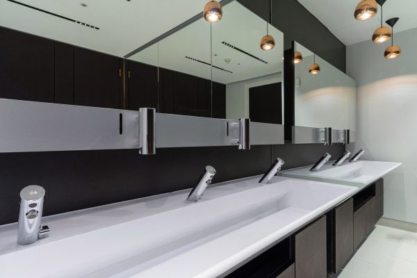 Contemporary refurbished restroom with updated counters, dark cabinetry, expansive mirrored walls, and stylish pendant lighting.