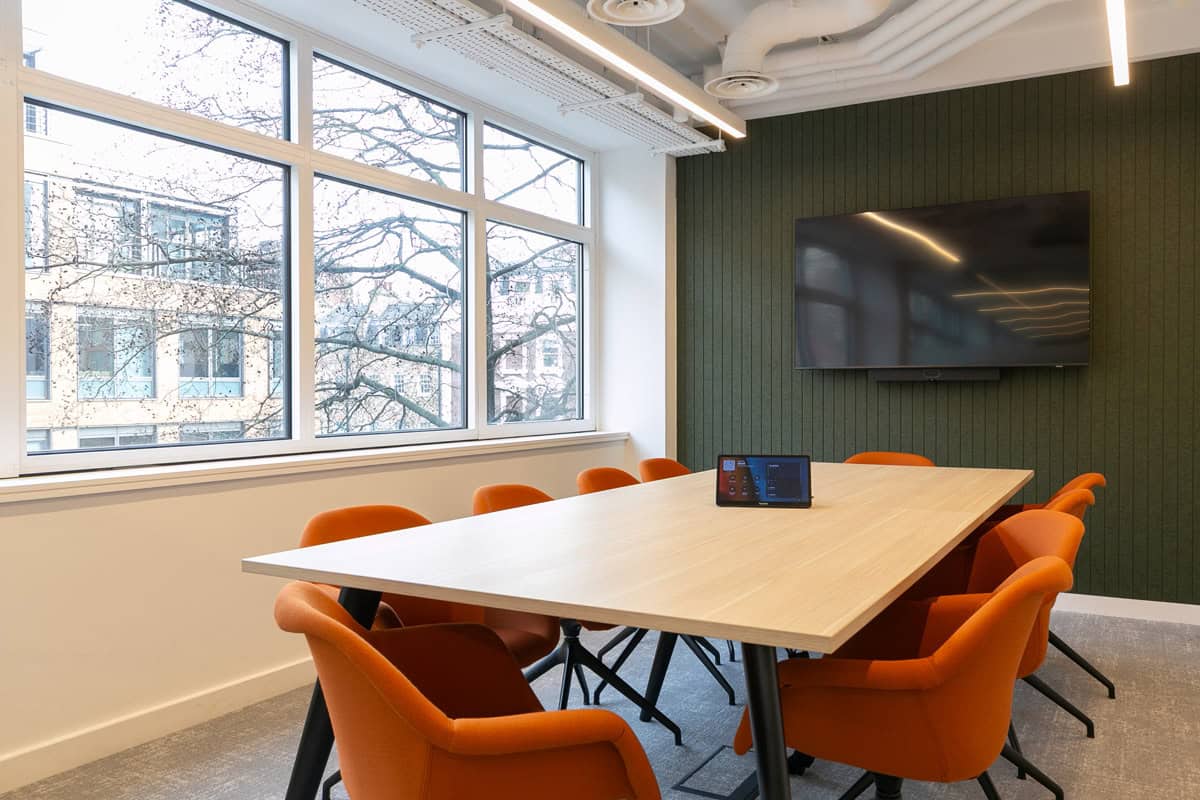 Refurbished meeting room featuring a large timber meeting table, bright orange upholstered chairs, upgraded acoustic wall panelling, and integrated AV screen as part of a modern office fit‑out.
