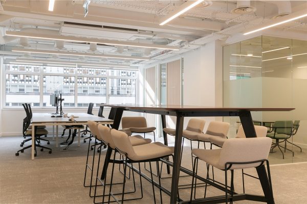 Open‑plan refurbished workspace featuring new ergonomic desks, high breakout table with stools, and exposed ceiling services for a modern industrial aesthetic.