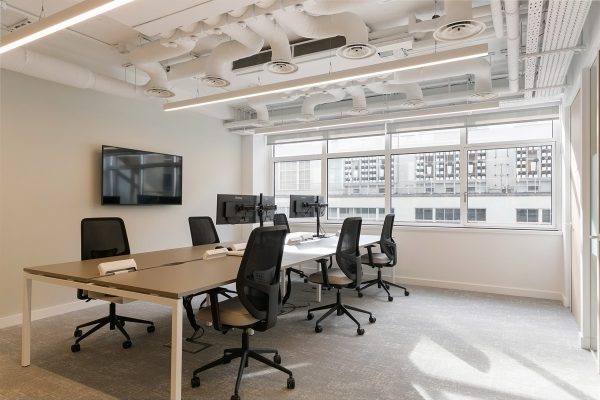 Refurbished open‑plan workspace fitted with modern desks, ergonomic seating, and integrated monitors beneath newly exposed and painted ceiling services.