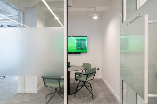 Compact meeting room created through new glass partitioning, furnished with soft green chairs and AV screen as part of a flexible workspace fit‑out.