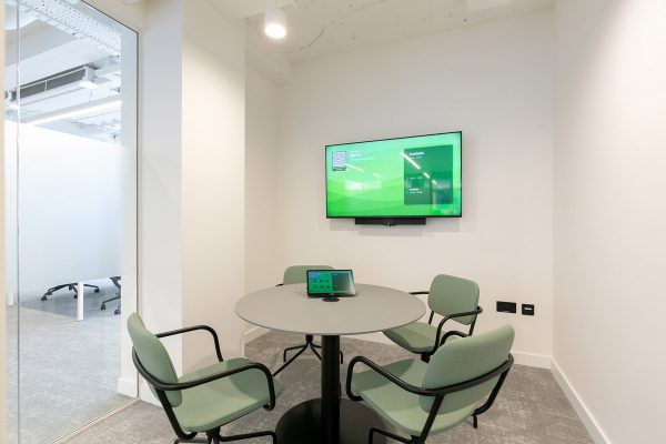 Refurbished focus room featuring a new round table, soft seating, and wall‑mounted screen for video calls within the upgraded workspace.