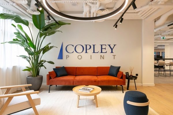 Refurbished reception area showcasing a statement orange sofa, biophilic planting, and branded wall signage as part of a contemporary fit‑out.