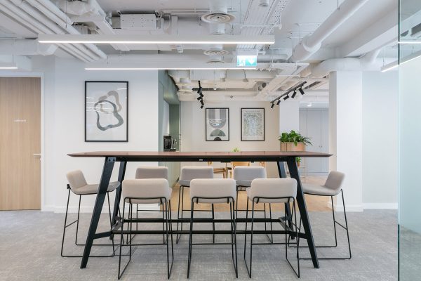 Communal collaboration zone fitted with a tall bench table, modern stools, and upgraded lighting as part of the open‑plan office refurbishment.