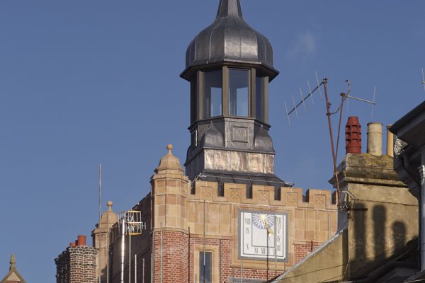 Refurbished heritage rooftop structure with reinstated cupola, glazed lantern and decorative weather vane, set above restored brickwork and stone façade, with retained clock feature and upgraded roofline integrating modern services discreetly.