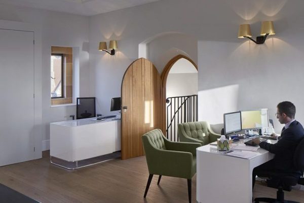 CAT B fit-out within a refurbished historic space, featuring a contemporary office layout with bespoke joinery, timber floors, and integrated LED lighting, complemented by restored architectural details including arched doorways and a central glazed roof lantern providing natural light.