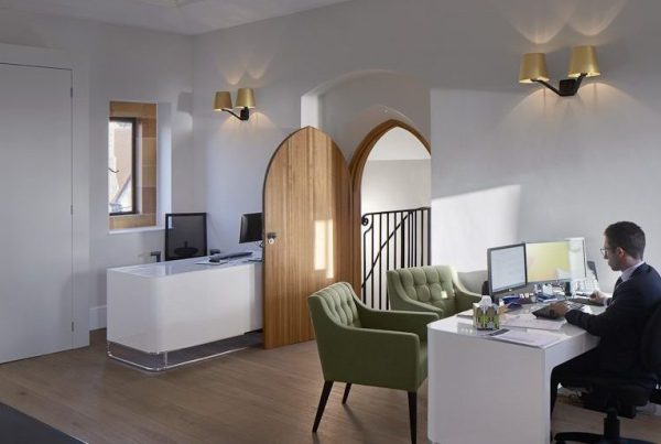 CAT B fit-out within a refurbished historic space, featuring a contemporary office layout with bespoke joinery, timber floors, and integrated LED lighting, complemented by restored architectural details including arched doorways and a central glazed roof lantern providing natural light.